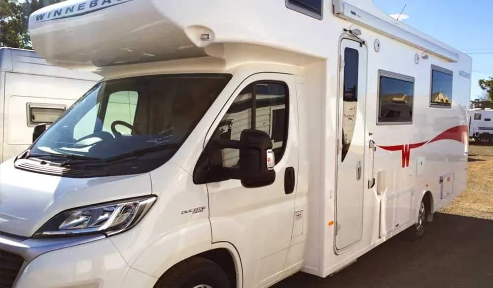 A Winnebago motorhome parked in a row of vans on the Kennedy RV yard