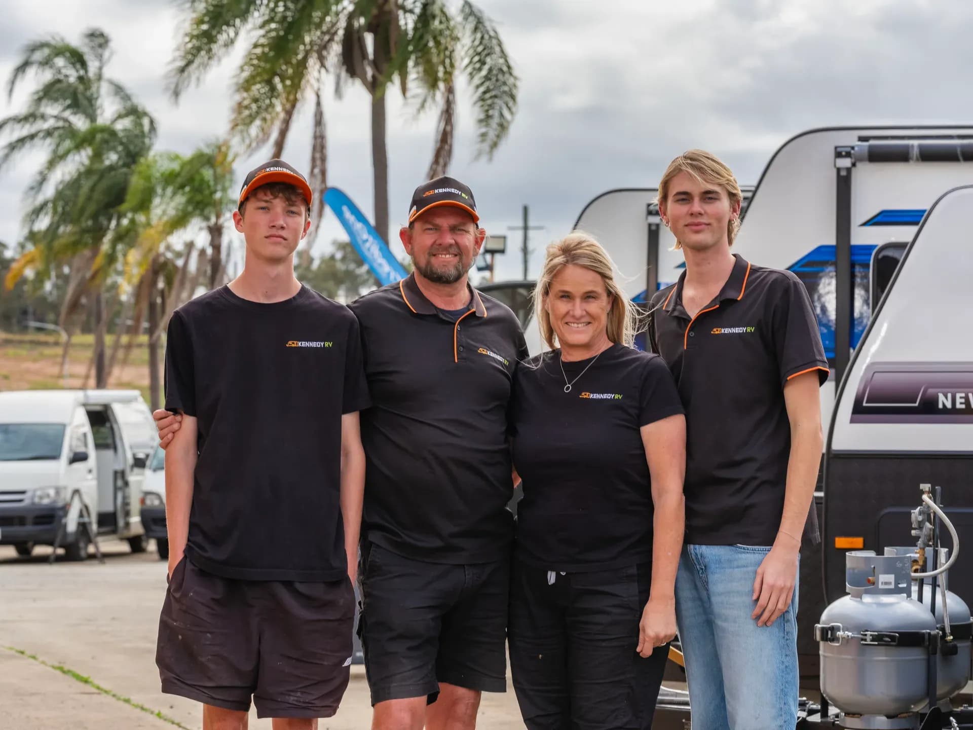 Four Kennedy RV team members in branded shirts standing together in front of a caravan on the yard
